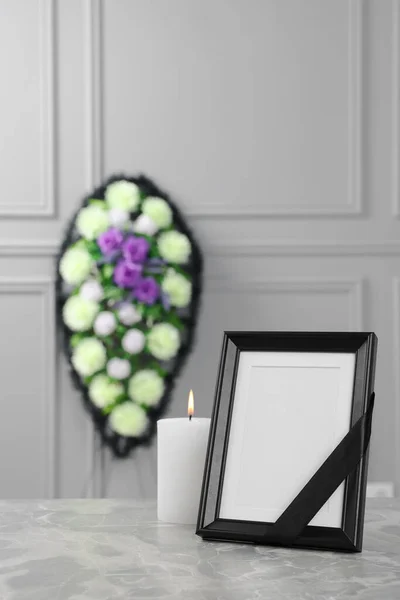 黒いリボンで写真フレーム ライトグレーのテーブルの上にろうそくを燃焼し 室内の壁の近くにプラスチックの花の花輪 葬儀の属性 — ストック写真
