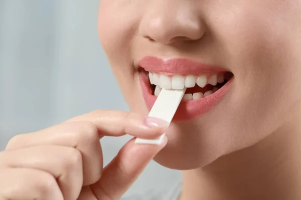 Woman putting chewing gum piece into mouth on blurred background, closeup