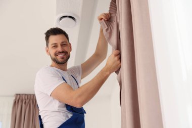 Üniformalı işçiler pencere perdelerini içeri asıyor.