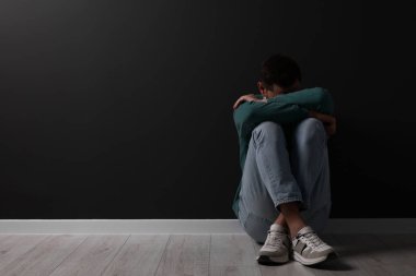 Kara duvarın yanında üzgün bir adam oturuyor. Metin için boşluk