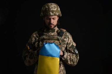Soldier in military uniform with Ukrainian flag on black background clipart
