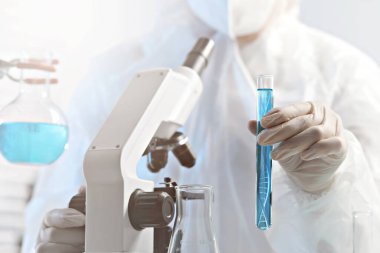 Genetik araştırma. Bilim adamları, laboratuarda sıvı ve DNA yapısını gösteren test tüpünü yakın çekimde tutuyor.
