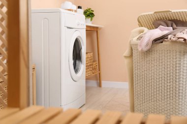 Laundry basket overfilled with clothes near washing machine in bathroom clipart