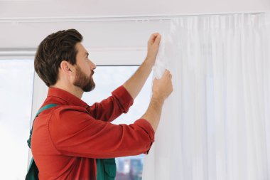 Üniformalı işçiler pencere perdelerini içeri asıyor.