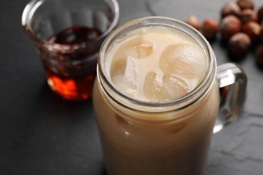 Mason kavanozu dolusu lezzetli buzlu kahve, şurup ve fındıklar siyah masada, yakın plan.