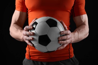 Siyah arka planda futbol topu olan atletik adam, yakın plan.