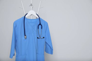 Tıbbi üniforma ve steteskop açık gri arka planda asılı duruyor. Metin için boşluk