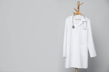 Tıbbi üniforma ve steteskop açık gri arka planda asılı duruyor. Metin için boşluk