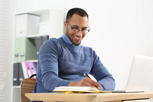 アフリカ系アメリカ人の男性がノートブックで木製のテーブルで書く笑顔 — ストック写真