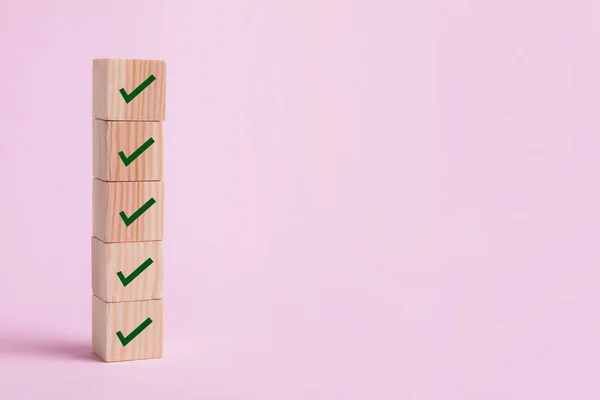 Stacked wooden cubes with check marks on pale pink background. Space for text