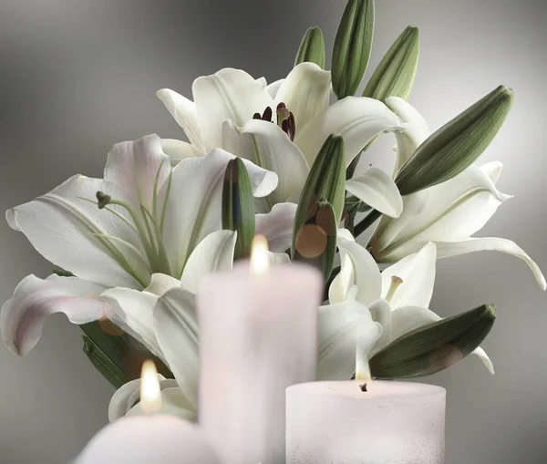 Funeral. Beautiful lilies and burning candles on light grey background, bokeh effect