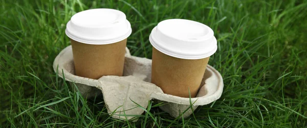 屋外の緑の芝生の上に段ボールホルダーにプラスチック蓋付きの持ち帰り紙コーヒーカップ — ストック写真