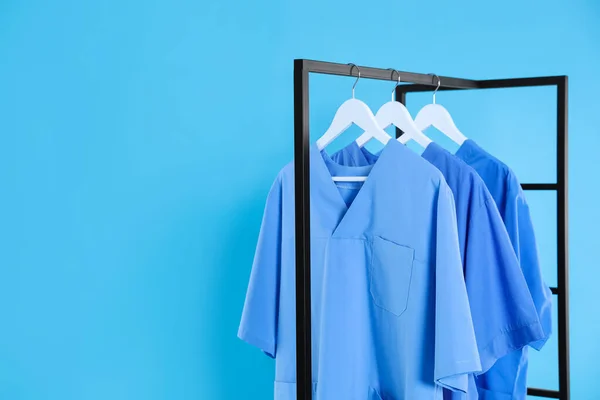 Medical uniforms on metal rack against light blue background. Space for text