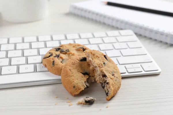 Chocolate chip cookies and keyboard on white wooden table, closeup