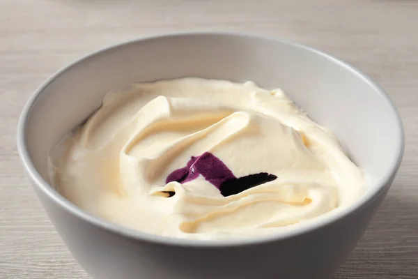 Bowl of cream with purple food coloring on white wooden table, closeup