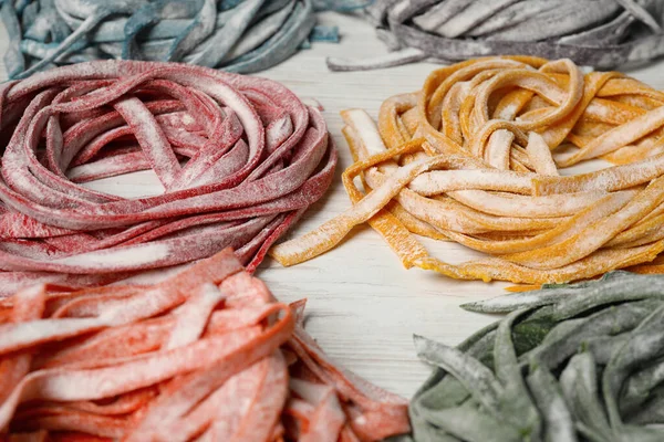 Rolled pasta painted with different food colorings on white wooden table, closeup
