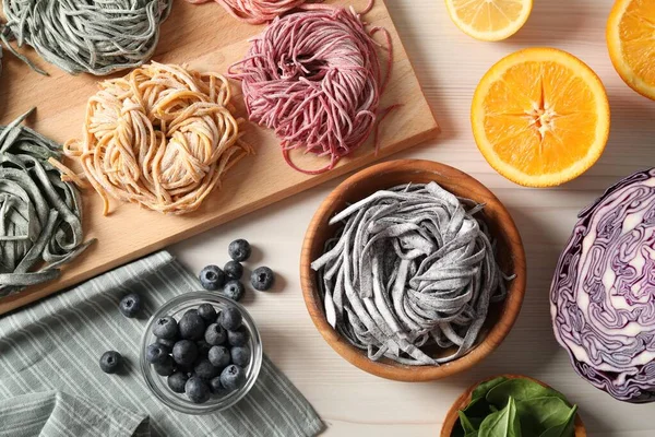 Rolled pasta painted with food colorings and ingredients on white wooden table, flat lay