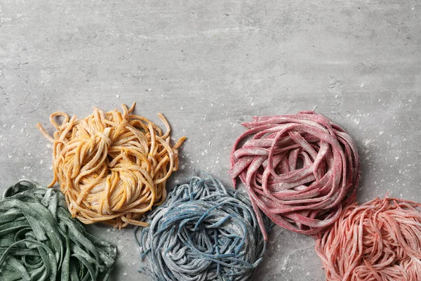Rolled pasta painted with food colorings on light grey table, flat lay. Space for text