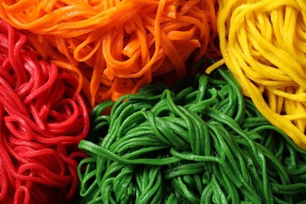Rolled spaghetti painted with different food colorings as background, closeup