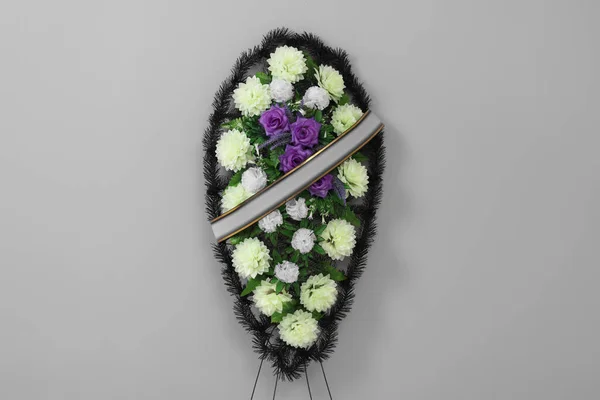 Funeral wreath of plastic flowers with ribbon on grey background