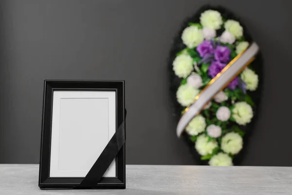 光のテーブルの上に黒いリボンとグレーの壁の近くの花の花輪を持つ写真フレーム室内 テキストのためのスペース 葬儀の属性 — ストック写真