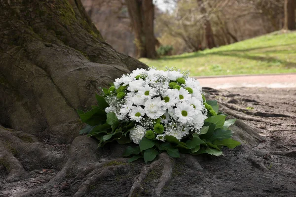 Funeral wreath of flowers near tree outdoors