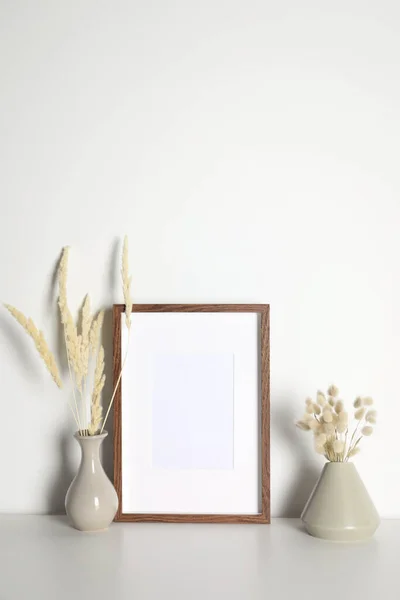 白いテーブルの上に乾いた装飾的なスパイクを持つ空の写真フレームと花瓶 デザインのためのモックアップ — ストック写真