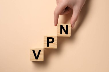 Kadın, bej arka planda tahta küplerle VPN kısaltması yapıyor.