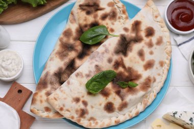 Lezzetli peynirli calzones, fesleğen ve soslar beyaz ahşap masada, düz yatıyordu.
