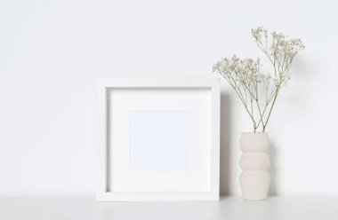 Boş fotoğraf çerçevesi ve vazo, dekoratif çingene çiçekleri beyaz masada. Tasarım için model