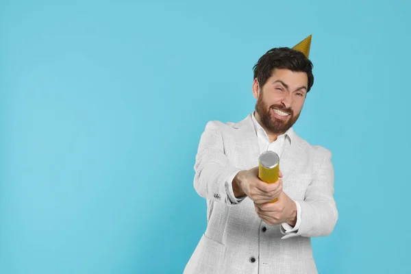Happy man with party popper on light blue background. Space for text