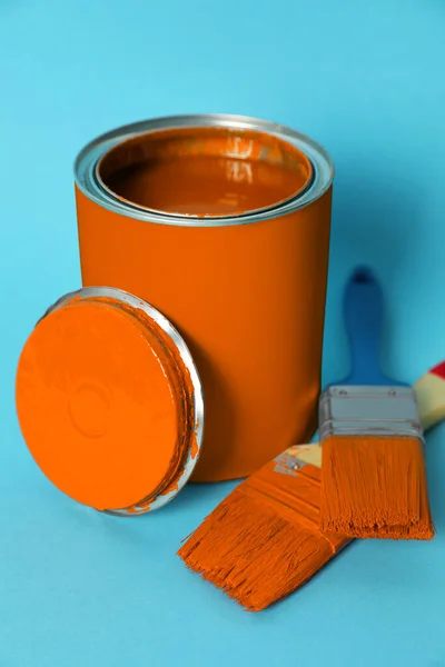 Can of orange paint and brushes on turquoise background