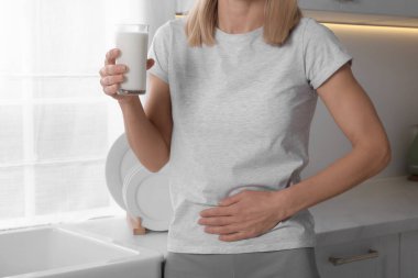 Woman with glass of milk suffering from lactose intolerance in kitchen, closeup clipart