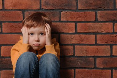 Upset boy sitting near brick wall, space for text. Children's bullying clipart