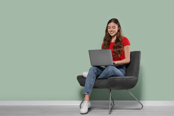 Щаслива Жінка Ноутбуком Сидить Кріслі Біля Блідо Зеленої Стіни Приміщенні — стокове фото