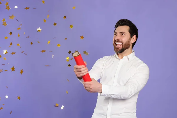 Happy man blowing up party popper on violet background