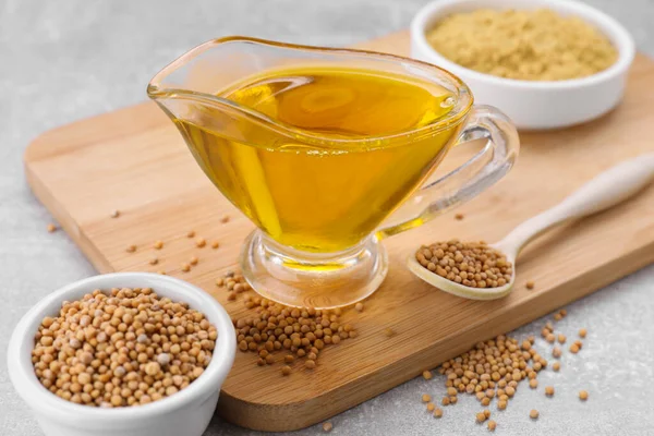 stock image Jug of natural oil, mustard seeds and powder on light grey , closeup