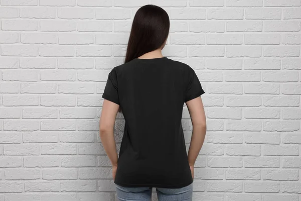 Woman wearing stylish black T-shirt near white brick wall, back view