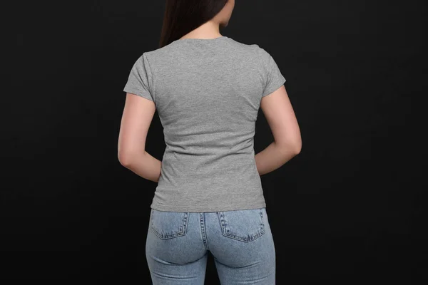 Woman wearing grey t-shirt on black background, back view