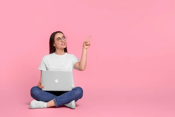 Smiling young woman with laptop on pink background, space for text