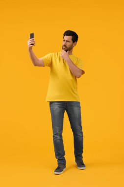 Sarı arka planda akıllı telefonlu bir adam selfie çekiyor.