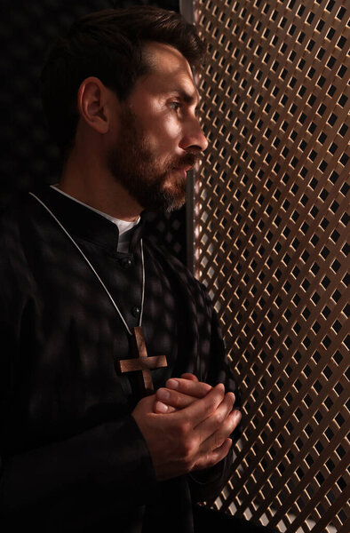 Catholic priest wearing cassock in confessional booth