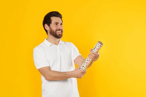 Happy man with party popper on yellow background. Space for text