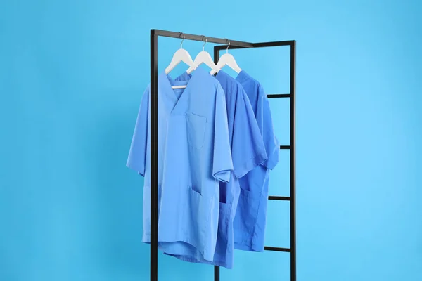 Medical uniforms on metal rack against light blue background