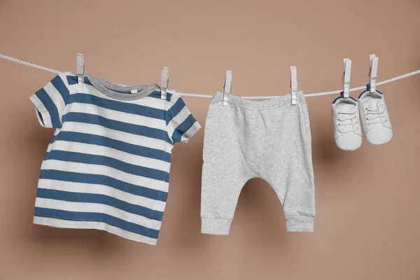 茶色の背景に洗濯ラインにかかってかわいい小さな赤ちゃんの靴と服 — ストック写真