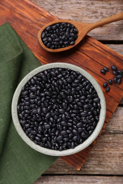 stock image Bowl and spoon of raw black beans on wooden table, flat lay