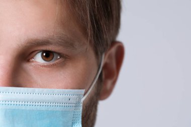 Açık gri arka planda koruyucu maskesi olan doktor ya da tıp asistanı (erkek hemşire), yakın plan. Metin için boşluk