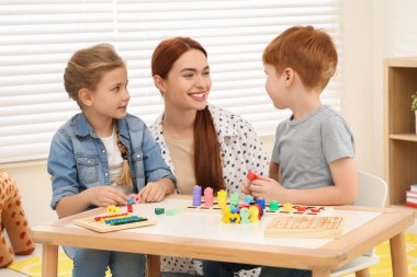 Mutlu anne ve çocuklar odadaki masada farklı matematik oyun setleriyle oynuyorlar. Matematiği zevkle çalış