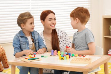Happy mother and children playing with different math game kits at desk in room. Study mathematics with pleasure clipart