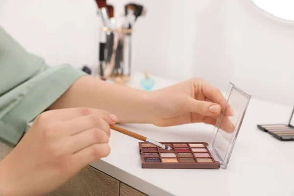 Woman with eyeshadow palette and brush at dressing table indoors, closeup